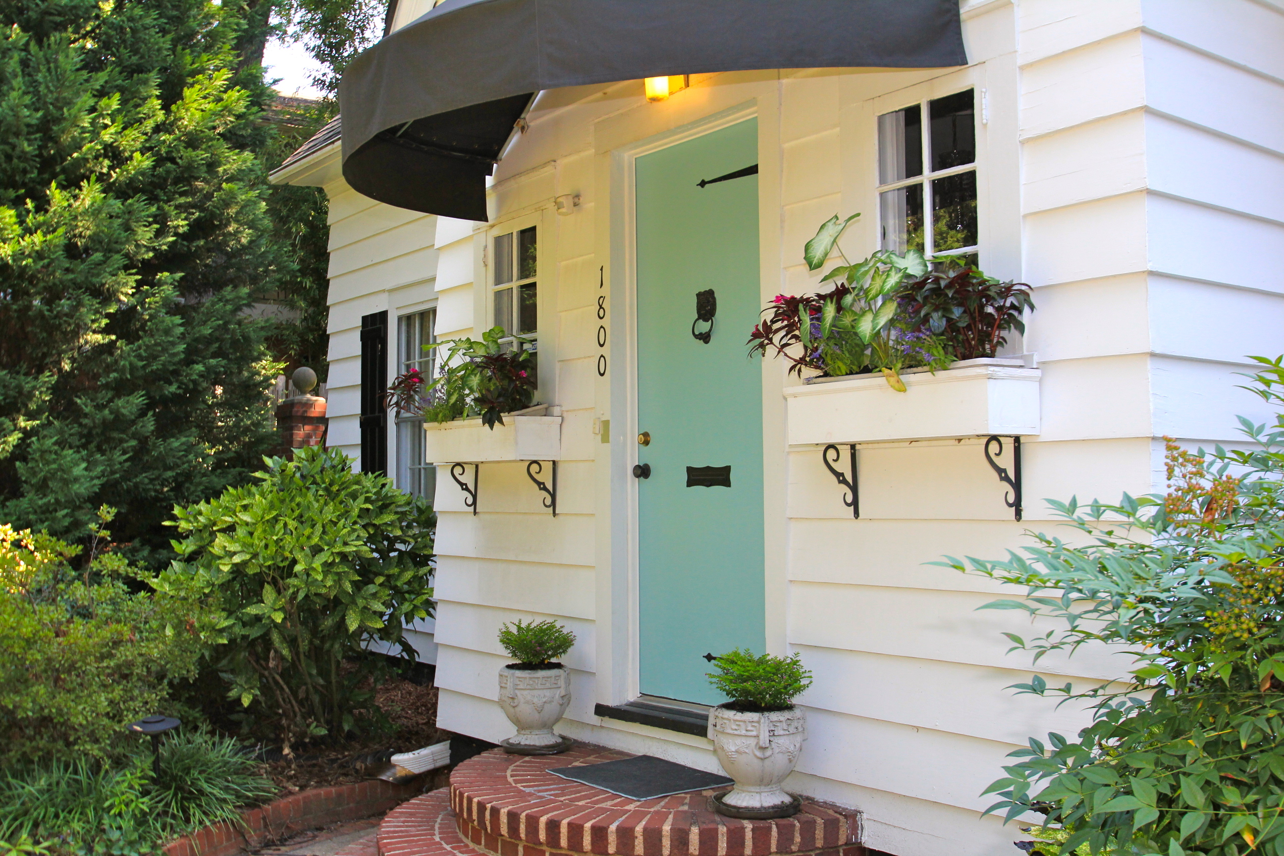 White siding home with blue front door white window boxes with plants potted plants by front door and brick steps