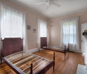 Bedroom with pink walls windows with white curtains white baseboards and wood floors two twin beds fireplace with white mantle