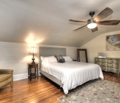 Bedroom with beige walls dark wood ceiling fan white baseboards wood floors green floral rug leather armchair