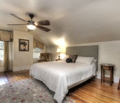 Bedroom with beige walls dark wood ceiling fan white baseboards wood floors windows with yellow curtains bed with white bedding