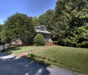 Home with trees in front yard brick paved walkway gray shingle home with screened in porch