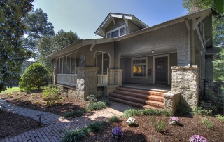 Home with gray shingles stone details around columns screened in front porch brick steps and walkway