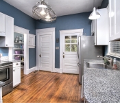 Kitchen with blue walls white baseboards wood floors white cabinets with gray granite countertops stainless steel appliances and window with white blinds