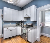 Kitchen with blue walls white baseboards wood floors white cabinets with gray granite countertops stainless steel oven and window with white blinds
