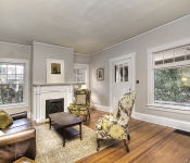 Living room with light gray walls fireplace with white painted brick and white mantle white baseboards and wood floors white trim windows and white door