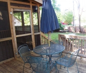 Wooden back deck with green metal outdoor table and chairs and blue umbrella