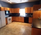 Kitchen with dark blue walls white fridge and oven and black dishwasher brown tile flooring brown wood cabinets and black countertops