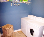 Laundry room with white washer and dryer brown tile floors blue walls with white baseboards brown laundry hamper and white wire shelf