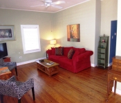 Living room with light green walls white ceiling fan white baseboards and wood floors red sofa and black and white chairs