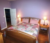 Bedroom with purple walls white baseboards wood floors and wooden bed and nightstand with floral patchwork quilt