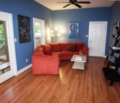 Living room with blue walls wood floors white baseboards and black ceiling fan two glass doors to backyard and orange sectional sofa