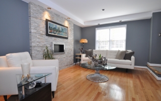 Living room with gray walls white baseboards wood floors windows with white blinds accent wall with gray brick and white leather sofa and chair