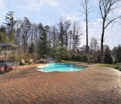 Built in pool with bricks around it stone waterfall with trees around it lounge chairs and dining table with umbrella and chairs