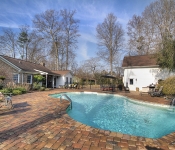 Backyard of brown brick home with built in pool with bricks around it and stone waterfall white siding garage