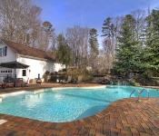 Backyard of brown brick home with built in pool with bricks around it and stone waterfall white siding garage