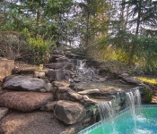 Built in pool with bricks around it and stone waterfall with trees around it