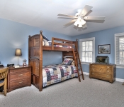 Bedroom with blue walls white baseboards white ceiling fan two windows with white blinds carpet flooring wood bunk beds