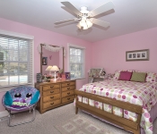 Bedroom with pink walls white ceiling fan two windows with white blinds carpet floors wood bed and dresser with pink details