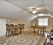 Attic with brown walls popcorn ceiling with white ceiling fan wood floors white baseboards pool table wood table and chairs