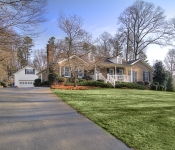 Brick home with black shutters front porch with white railings and white columns large front yard driveway to white siding garage in back