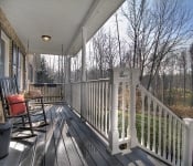 Front porch with black floor white railings white columns brick house with black shutters black rocking chair and swing