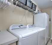 Laundry room with brown walls white wire shelf white washer and dryer white standing freezer and tile flooring