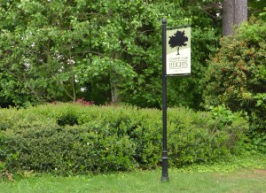 Green Country Club Heights sign on black metal post with green bushes and trees in background