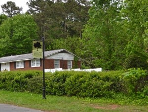 Green Country Club Heights sign on black metal post with green bushes and trees in background