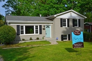 Gray painted brick split level home with black shutters light blue front door and brown and blue Savvy Sign in the front yard