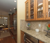 Bar area in kitchen with wood cabinets and brown granite countertop and brown tile backsplash built in wine fridge