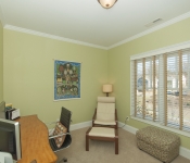 Home office with light green walls white baseboards window with white and light brown blinds wood desk and black desk chair