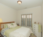 Bedroom with beige walls white baseboards window with white and light brown blinds wood bed and white dresser