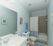 Bathroom with light blue walls white baseboards brown tile floor and in shower white cabinets white countertop and white toilet