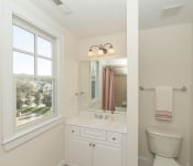 Bathroom with beige walls window by sink with white cabinets white countertop separate area with white toilet