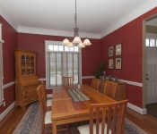 Dining room with bright red walls white baseboards wood floors wood dining room tale chairs and hutch two windows with white blinds