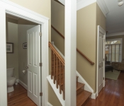 Hallway with light brown walls white baseboards white column wood stairs with wood railing and banister door open to bathroom