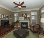 Living room with brown walls white baseboards brown ceiling fan wood floors gray fireplace with white mantle widows with white and light brown blinds