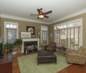 Living room with brown walls white baseboards brown ceiling fan wood floors gray fireplace with white mantle widows with white and light brown blinds