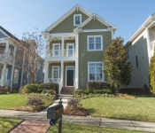 Three story green siding home with green shingles white trim windows two story front porches with white railings and columns black front door