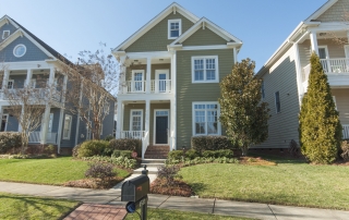 Three story green siding home with green shingles white trim windows two story front porches with white railings and columns black front door