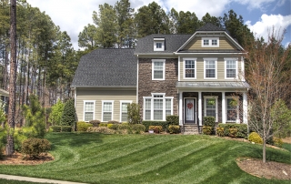 Three story home with brown siding brown shingles and brown stone with white framed windows front porch with metal railing and white posts