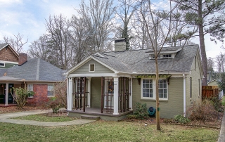 Painted green brick home with white windows and white front door brown front porch with white columns brown wood railing