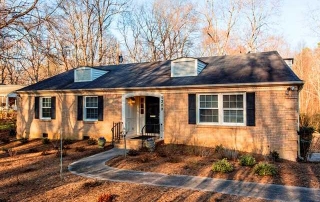 Light brown brick home with black shutters black front door steps to front door with iron railing