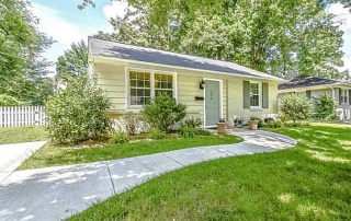 Yellow siding home with two white frame windows green shutters green front door white picket fence in backyard