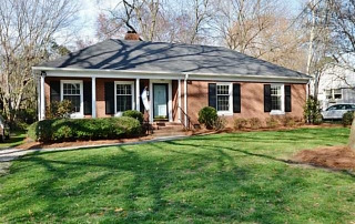 Brown brick home with black shutters blue front door front porch with three white columns flag hanging from porch