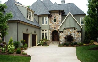 Large two story green stucco home with stone details yellow trim windows two dark wood garage doors dark wood front door