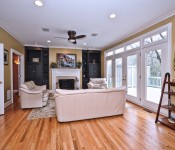Living room with wood floors white trim yellow walls wood ceiling fan with white leather sofas with black built in bookshelves and fireplace with white mantle