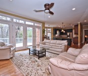 Living room with wood floors white trim yellow walls wood ceiling fan with white leather sofas and open to kitchen