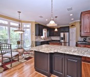 Kitchen with half black cabinets and half brown cabinets stainless steel appliance wood floors gray granite countertops and black granite countertops