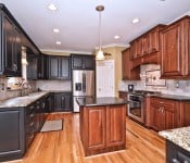 Kitchen with half black cabinets and half brown cabinets stainless steel appliance wood floors gray granite countertops and black granite countertops